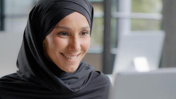 carino positivo arabo donna nel hijab sembra a il computer portatile schermo sorridente Guardando divertente video su Internet legge bene notizia contento femmina professionale manager Lavorando su computer nel ufficio prende simpatico notifica foto