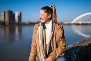 bellissimo donna nel caldo capi di abbigliamento gode riposo di il fiume su un' soleggiato inverno giorno. foto