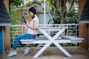 giovane asiatico ragazza lettura un' libro a il terrazze foto