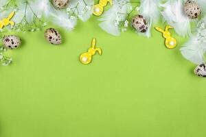 Pasqua confine piatto posare con Quaglia uova, primavera fiori, giallo coniglietti e bianca piume su un' verde sfondo. superiore Visualizza. copia spazio. foto