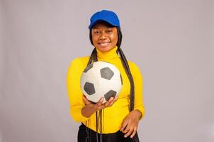 bellissimo africano calcio fan sorridente come lei tenuto palla su sua Telefono foto