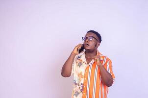 giovane nero africano ragazzo in piedi su un' bianca studio parete fabbricazione chiamate con il suo mobile Telefono ridendo su foto