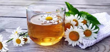 primo piano aromatico del tè alla camomilla in una tazza di vetro su un fondo di legno. natura morta estiva con fiori di campo e bevanda a base di erbe medicinali. sfondo floreale. foto