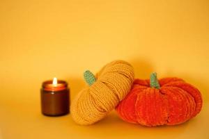 due zucche lavorate a maglia e una candela di soia accesa in un barattolo di vetro scuro su sfondo giallo. preparando per halloween. rilassati e calmati. foto