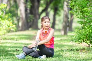 atleta giovane bellissimo donna con un' plastica acqua bottiglia e cuffie a il verde parco, sportiva potabile acqua dopo Lavorando su esercizio foto