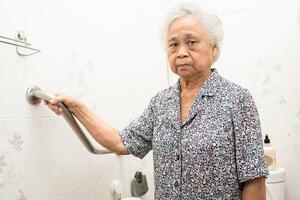 asiatico anziano donna uso gabinetto bagno maniglia sicurezza, salutare forte medico concetto. foto