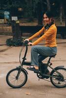 contento giovane asiatico donna mentre equitazione un' bicicletta nel un' città parco. lei sorrise utilizzando il bicicletta di trasporto. l'ambiente amichevole concetto. foto