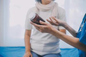 asiatico donna infermiera Tenere un' medicina bottiglia e telling informazione per asiatico anziano donna prima amministrazione farmaco. badante visitare a casa. casa Salute cura e assistenza infermieristica casa concetto. foto