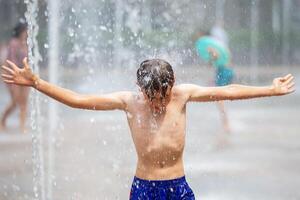 un' ragazzo bagna nel un' Fontana nel il calore e si raffredda via su un' caldo giorno. clima riscaldamento. foto