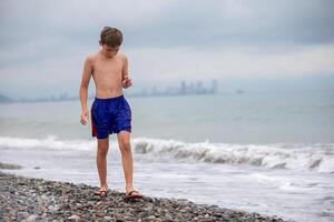 il ragazzo passeggiate lungo il roccioso riva di il mare. foto