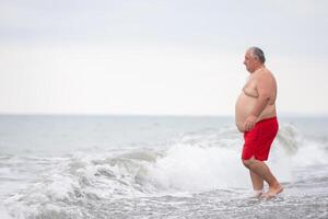 un sovrappeso anziano uomo è riposo su il mare. foto