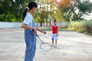 asiatico ragazza e ragazzo giocare badminton all'aperto a il parco insieme su vacanza. morbido e selettivo messa a fuoco. foto