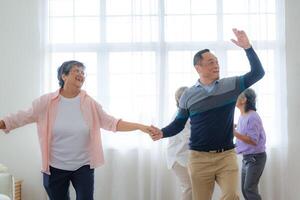 asiatico più vecchio maschio e femmine persone danza con loro partner su un' danza pavimento nel vivente spazio. contento più vecchio coppia l'esecuzione ottenere esercizio. gioioso spensierato pensionato anziano amici godendo rilassamento foto