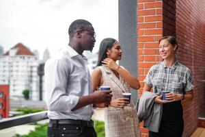 squadra di attività commerciale persone inteligente uomo e donne In piedi a all'aperto terrazza edificio e parlare insieme con prima colazione cibo e caffè su il mano nel bene sensazione con città spazio costruzione. attività commerciale mattina. foto