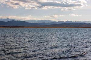 blu calma acqua nel issykkul lago con montagne su sfondo a autunno pomeriggio foto