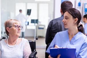 infermiera limatura documenti mentre parlando con Disabilitato anziano donna nel ospedale in attesa la zona. paziente chiede per direzione a ospedale ricezione. foto