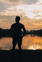 indietro Visualizza silhouette di un' corridore uomo in esecuzione su il spiaggia a tramonto con sole nel il sfondo foto