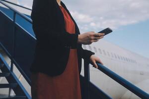 giovane asiatico donna nel internazionale aeroporto, utilizzando mobile smartphone e controllo volo a il volo informazione tavola foto