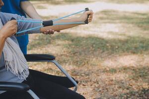 giovane infermiera o fisioterapista nel scrub porzione un' contento pensionato vecchio donna fare fitness esercizi con leggero peso manubri a casa. concetto di fisioterapia per gli anziani foto