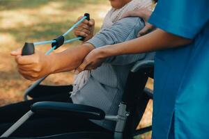 giovane infermiera o fisioterapista nel scrub porzione un' contento pensionato vecchio donna fare fitness esercizi con leggero peso manubri a casa. concetto di fisioterapia per gli anziani foto