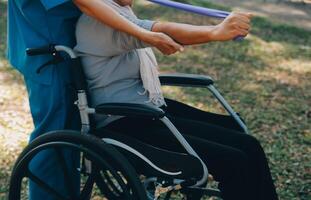 giovane infermiera o fisioterapista nel scrub porzione un' contento pensionato vecchio donna fare fitness esercizi con leggero peso manubri a casa. concetto di fisioterapia per gli anziani foto