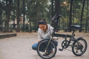 contento asiatico giovane donna camminare e cavalcata bicicletta nel parco, strada città sua sorridente utilizzando bicicletta di trasporto, eco amichevole, persone stile di vita concetto. foto