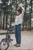 contento asiatico giovane donna camminare e cavalcata bicicletta nel parco, strada città sua sorridente utilizzando bicicletta di trasporto, eco amichevole, persone stile di vita concetto. foto