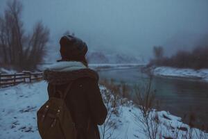 ai generato un' ragazza con un' zaino sta su il bordo di un' congelato fiume. foto
