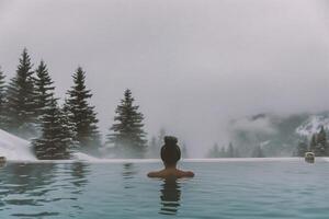 ai generato donna rilassante nel all'aperto nuoto piscina con nebbioso montagne nel il sfondo foto