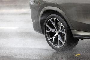 pioggia acqua spruzzi flussi a partire dal ruote di grigio auto quello in movimento veloce su asfalto strada foto