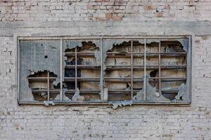 vecchio finestra coperto con strappato ruberoid Materiale e vecchio di legno tavole su bianca mattone parete di un abbandonato edificio foto