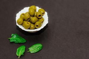 verde in scatola olive nel un' bianca ciotola su un' nero tavolo foto