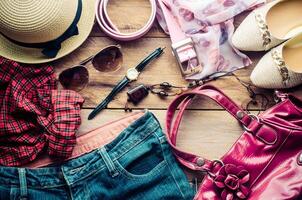 Accessori per adolescenziale ragazza su sua vacanza, cappello, elegante per estate occhiali da sole, pelle Borsa, scarpe e costume su di legno pavimento. foto