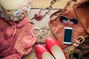 Accessori per adolescenziale ragazza su sua vacanza. cannuccia cappello, elegante occhiali da sole, Marrone pelle Borsa, rosso scarpe e costume su di legno pavimento. foto