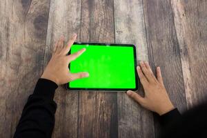 finto su di un' mano Tenere un ipad tavoletta con un' schermo verde contro un' di legno struttura sfondo foto