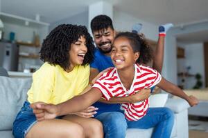 contento famiglia ritratto. gioioso madre, padre e loro carino figlia in posa nel vivente camera a casa, poco ragazza seduta su di papà giro, gratuito spazio foto