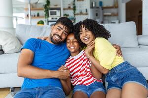 contento famiglia madre padre e bambino figlia ridendo e havig divertimento a casa. contento africano americano famiglia rilassante foto