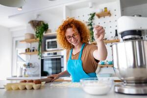 cottura al forno concetto. ritratto di gioioso donna impasto Impasto nel cucina interno, allegro femmina nel grembiule avendo divertimento mentre preparazione fatti in casa Pasticcino, foto