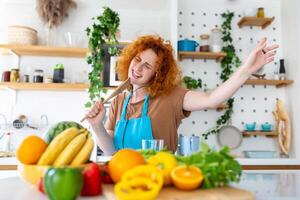 divertente bellissimo donna cantando in spatola, cucinando nel moderno cucina, Tenere spatola come microfono, ballare, ascoltando per musica, giocoso ragazza avendo divertimento con stoviglie, preparazione cibo. foto