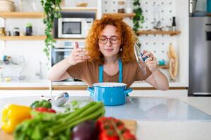 allegro giovane bella femmina nel grembiule preparare pranzo e odore piatto nel cucina a casa. donna cucinando cena per famiglia a nuovo ricetta a casa. foto