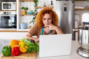 un' giovane donna impara per cucinare, lei orologi video ricette su un' il computer portatile nel il cucina e cucinare un' piatto . cucinando a casa concetto foto