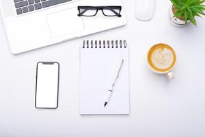 superiore Visualizza con Lavorando scrivania con laptop, cellulare, notebook matita caffè tazza e occhiali nel il ufficio. foto