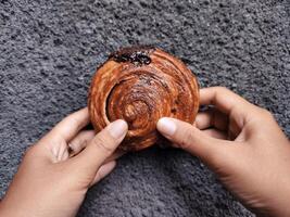 mani Tenere cromboloni, il giro brioche, nuovo York rotolo, un' virale Pasticcino combinando Cornetti e bomboloni su calcestruzzo parete sfondo. foto