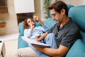 focalizzata giovane marito assunzione Appunti nel taccuino mentre seduta con moglie su divano foto