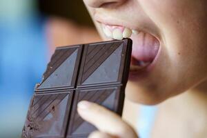 anonimo giovane ragazza con bocca Aperto di per mangiare cioccolato bar foto