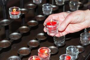 preghiera candele dentro un' cattolico Chiesa. un' donna di mano detiene un' candela. foto