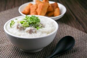 Maiale porridge con coriandolo e Zenzero o porridge è simile per riso porridge ma più morbido nel struttura. servito su un' di legno tavolo con patongko. per prima colazione nel il mattina o sera foto