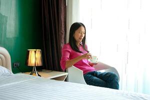 ritratto di bellissimo giovane asiatico donna Tenere tazza di mattina caffè nel bianca Camera da letto, felice, allegro, rilassante nel estate. tailandese asiatico trucco idee, bianca Camera da letto foto