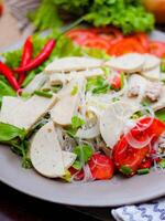 speziato bicchiere spaghetto insalata con vietnamita salsiccia servito nel un' grigio piatto mettere su un' di legno tavolo e vario verdure. foto