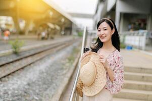 giovane asiatico donna viaggiatore con tessitura cestino in attesa per treno nel treno stazione. viaggio viaggio stile di vita, mondo viaggio esploratore o Asia estate turismo concetto. foto